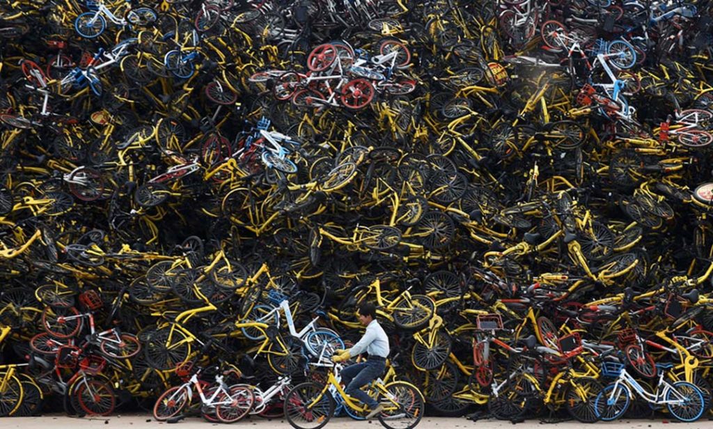 A worker rides a shared bicycle past piled-up shared bikes at a vacant lot in Xiamen, Fujian province, China December 13, 2017. Picture taken December 13, 2017. REUTERS/Stringer  ATTENTION EDITORS - THIS IMAGE WAS PROVIDED BY A THIRD PARTY. CHINA OUT.     TPX IMAGES OF THE DAY - RC16B19B1FA0