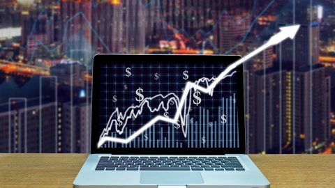 Stock exchange market trading graph over the screen of computer laptop on wood table over the photo blurred of trading graph background, business marketing trade concept