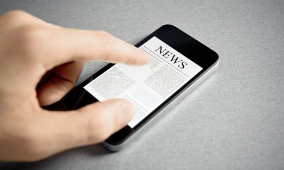 Man hand touch screen with news on contemporary mobile phone. Added a slight vignetting for dramatic effect and focus on the main headline.