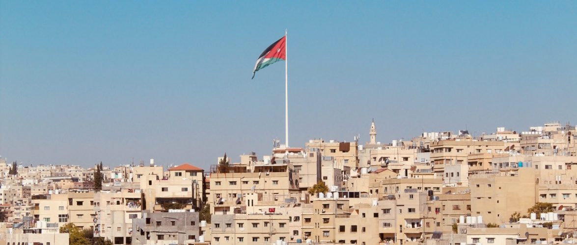 A Jordanian flag flutters above the cityscape. Photo by Who’s Denilo? on Unsplash.