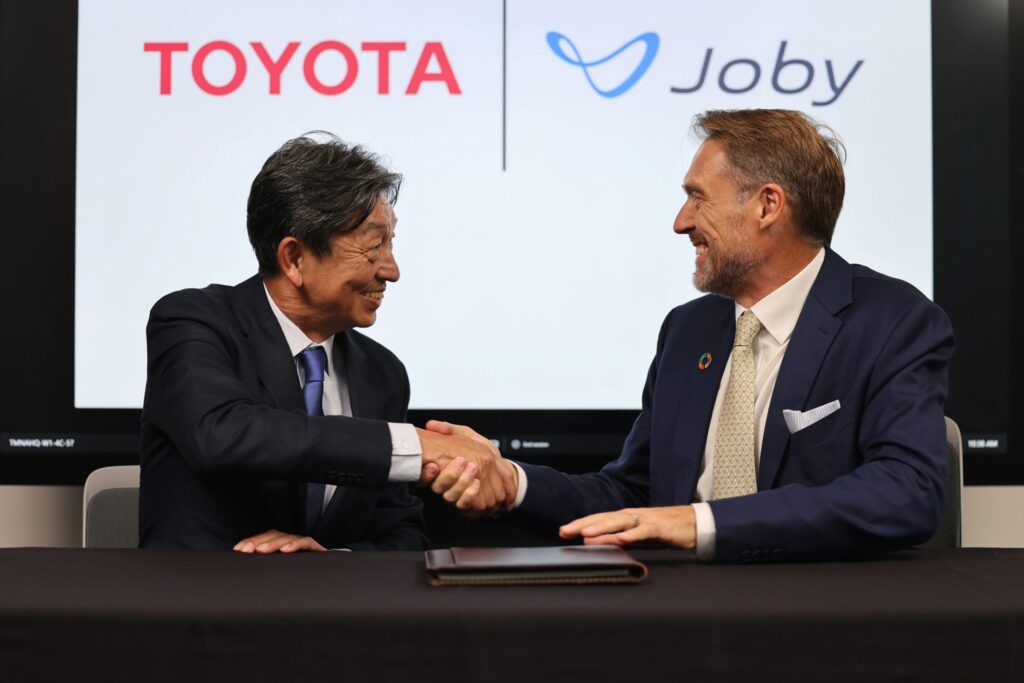 Photo of Tetsuo Ogawa (left), operating officer of Toyota Motor, shaking hands with JoeBen Bevirt, founder and CEO of Joby Aviation, during a signing ceremony to formalize Toyota’s investment in the electric air taxi company.