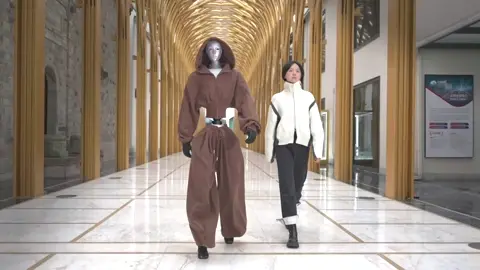 A catwalk sequence with Unitree's H2 robot dressed in costumes walking alongside human models.