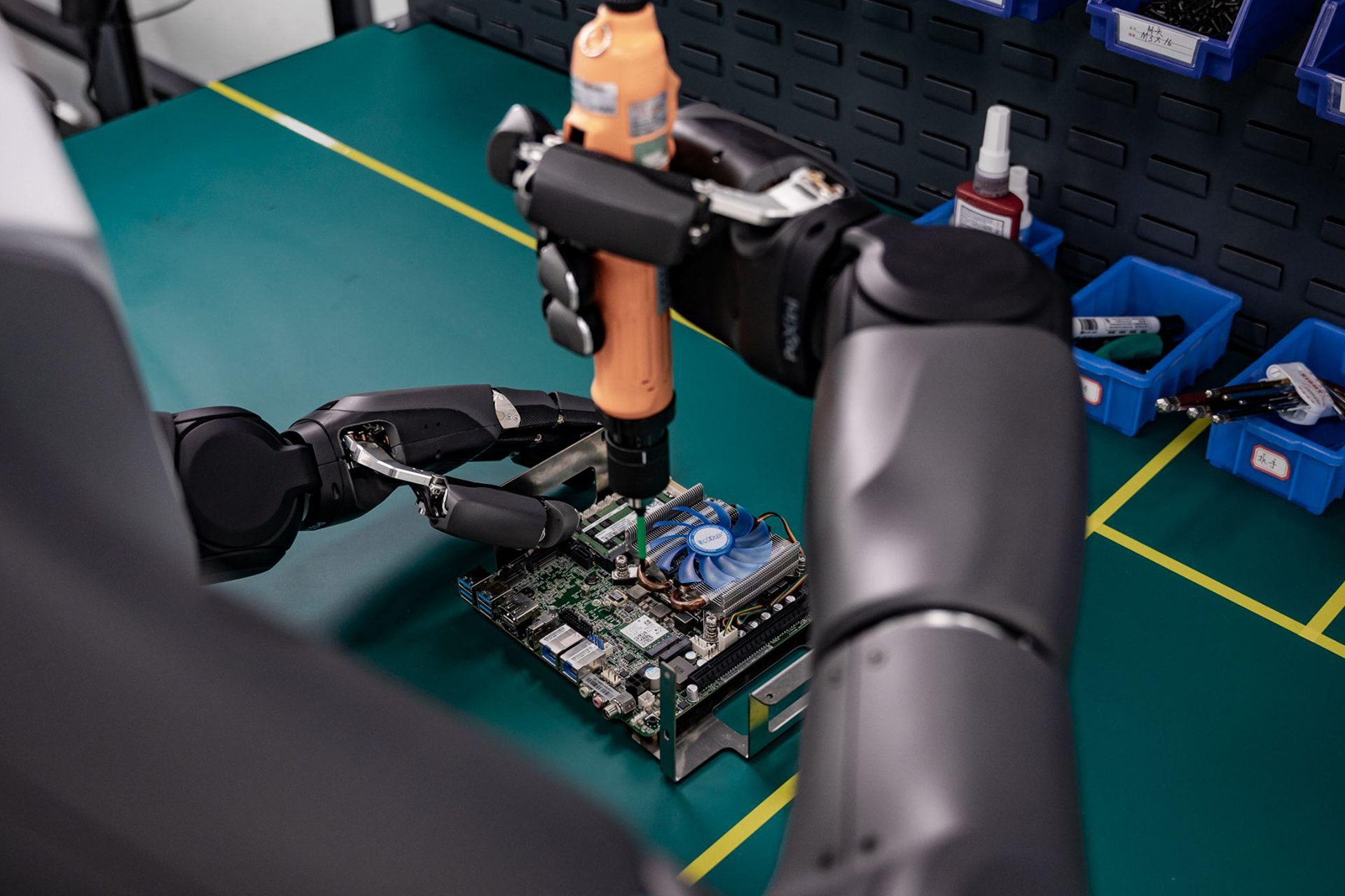 Photo of a humanoid robot performing a chip assembly task using a fixed arm and gripper configuration.