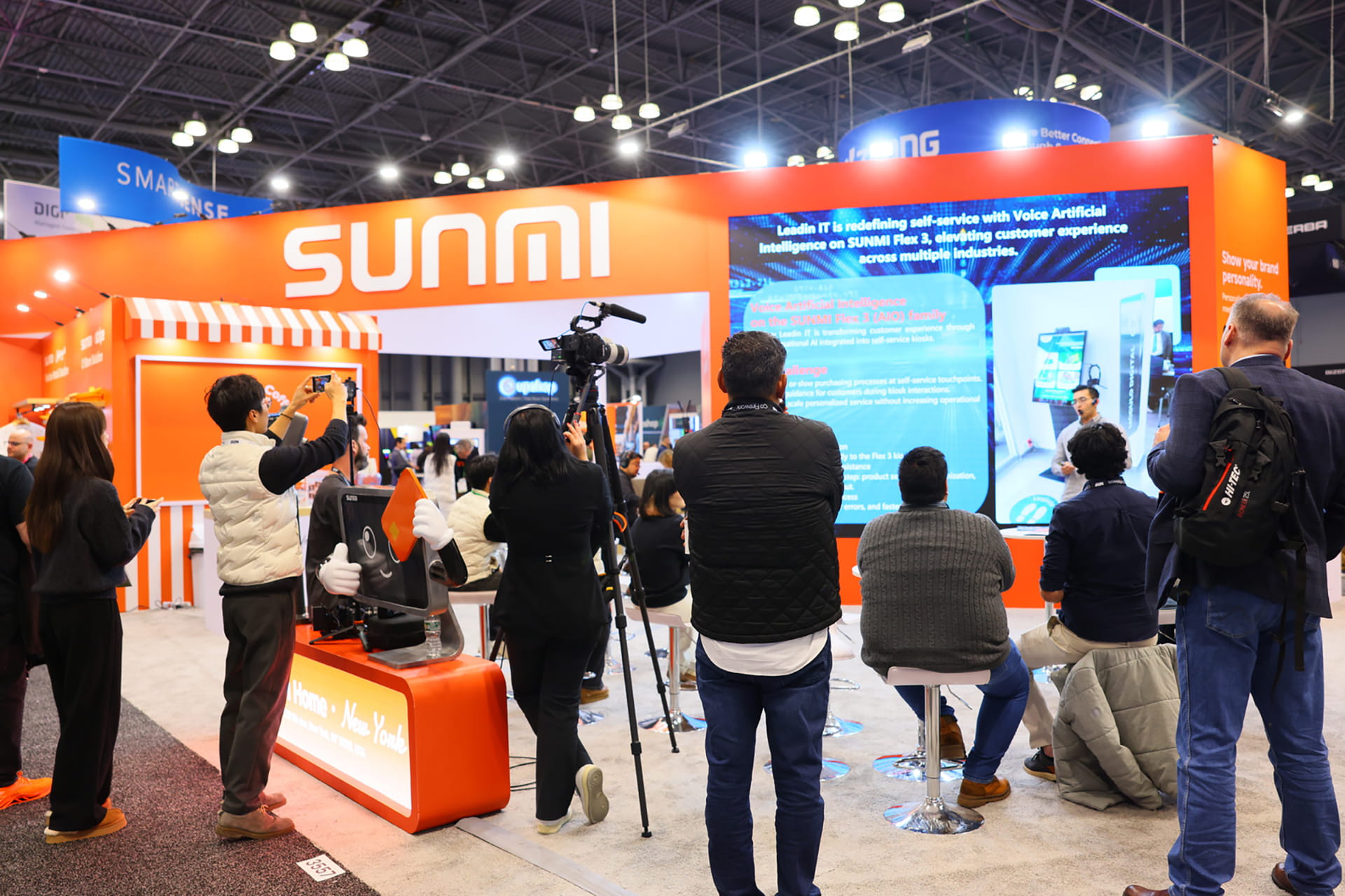 Photo shows NRF 2026 visitors at Sunmi's booth, watching a presentation about solutions developed by the company and its partners, including the Flex 3 interactive display.